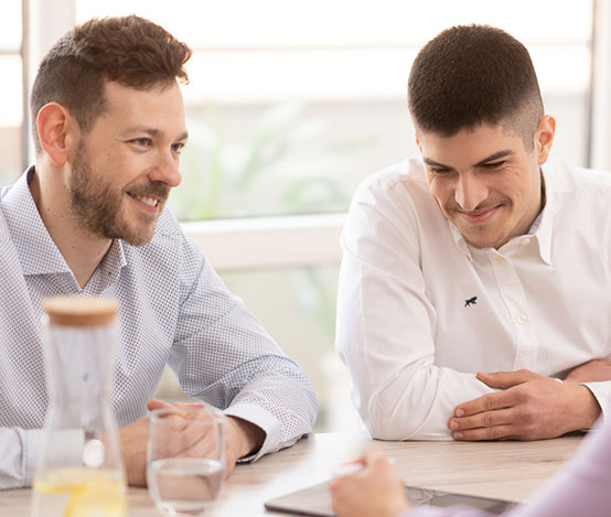 Männer in Business-Kleidung befinden sich im Gespräch mit einem Dienstleister und lächeln der Person zu.